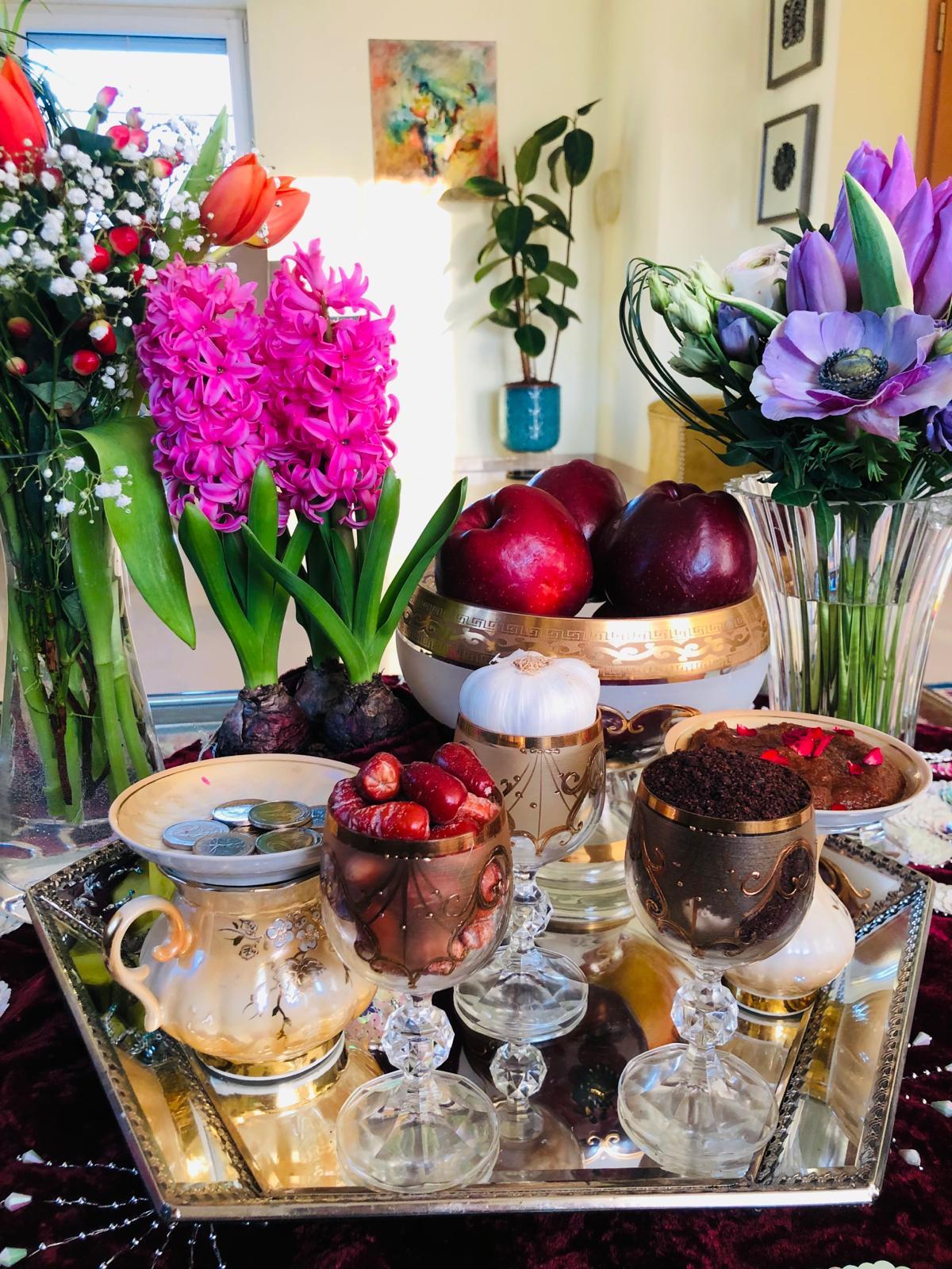 table decorated with spring flowers, bowl of apples, other dishes with colorful fruit, coins and other items 